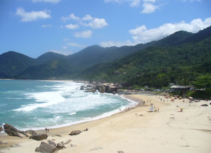 Retro Brazilian beach scene with sunlit sand, ocean waves, and lush green hills under a clear blue sky.