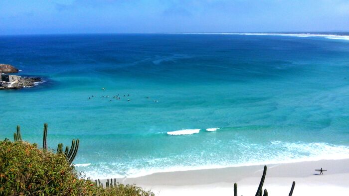 Retro Brazilian beach scene with turquoise ocean, white sand, and surfer, capturing sun, sand, and saudade.