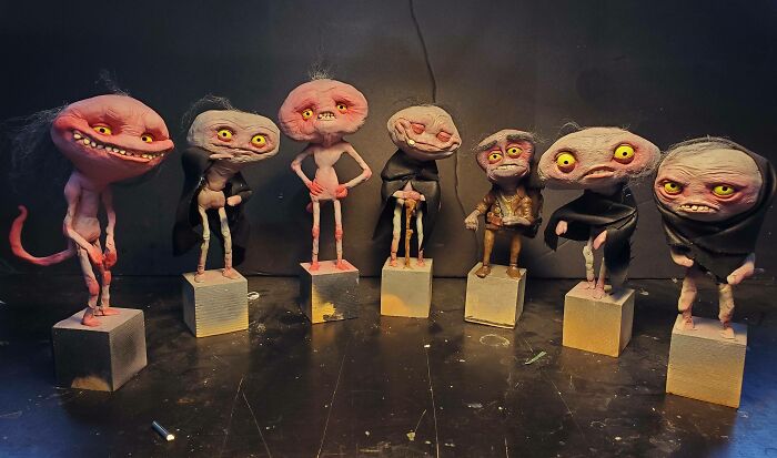 Seven quirky, eerie handmade crafts resembling small creatures with big eyes, standing on blocks.