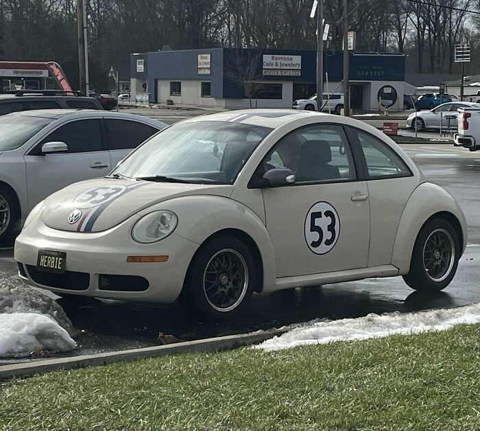 White Volkswagen Beetle with "53" decals, reminiscent of classic Herbie design, parked in a suburban area, evoking nostalgia.
