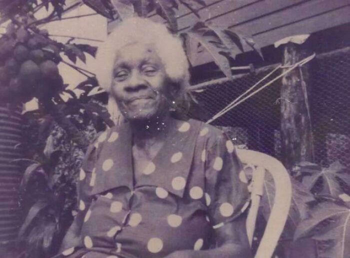 Elderly woman in a polka dot dress seated outdoors, offering a candid glimpse into the past not found in history books.