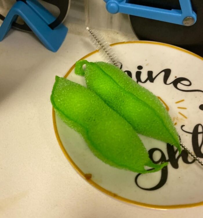 Two green dish sponges shaped like pea pods on a decorative plate, inject goofiness into your kitchen space.