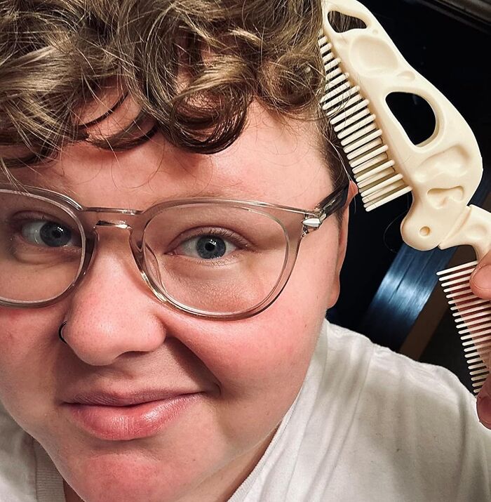 Person with glasses using a dinosaur-shaped comb, adding goofiness to their hair styling routine.