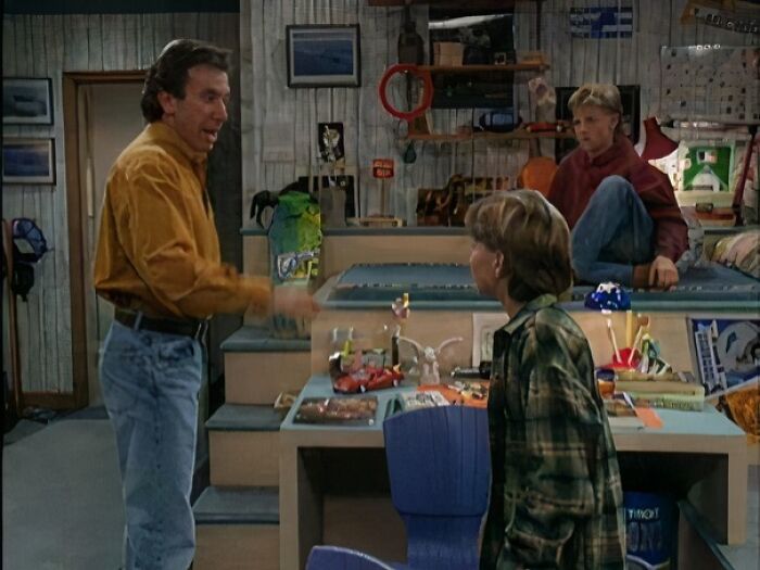 90s sitcom family scene in a cluttered bedroom with a man and two kids talking.