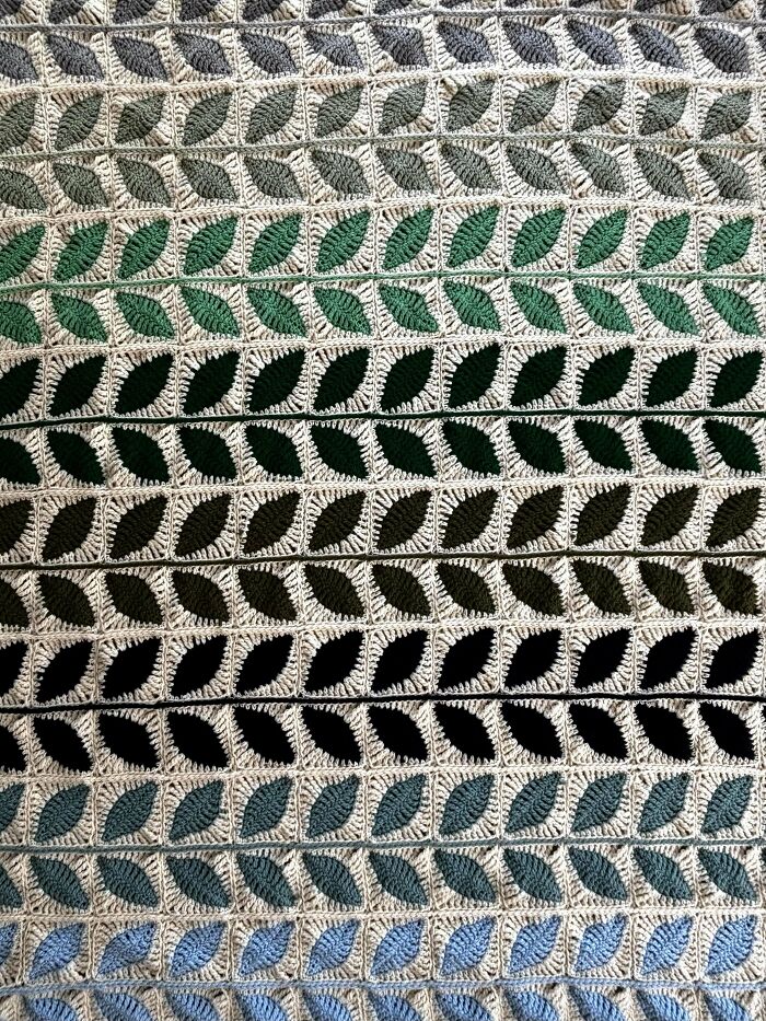 Crochet blanket with leaf patterns in various shades of green and blue, showcasing intricate crochet craftsmanship.
