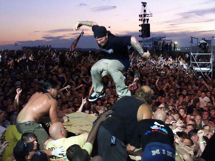Man leaping into a vibrant '90s concert crowd at sunset, embodying the wild '90s music scene.