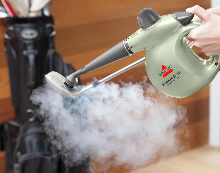 "Using a steam cleaner on golf clubs for a spring cleaning headstart, with vapor visibly removing dirt effectively."