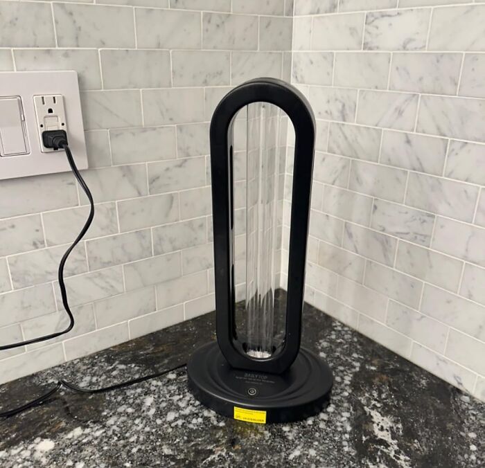 A sleek air purifier on a kitchen counter helps with spring cleaning headstart, plugged into a tiled backsplash outlet.