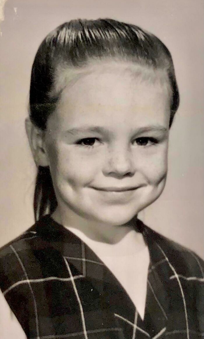Black and white portrait of a smiling young girl with dimples wearing a plaid dress, a candid glimpse into the past.