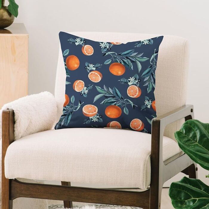 Cushion with orange fruit design from Society 6 on a beige armchair in a modern room.