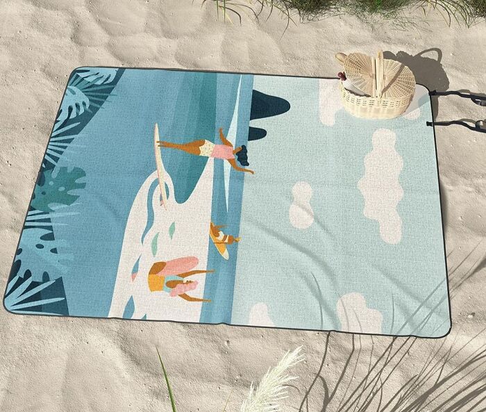 Beach-themed Society 6 towel on sand with picnic basket.