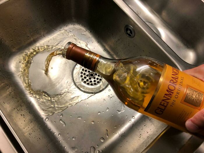 Person pouring whiskey into a sink, showcasing a life improvement choice from a popular discussion thread.