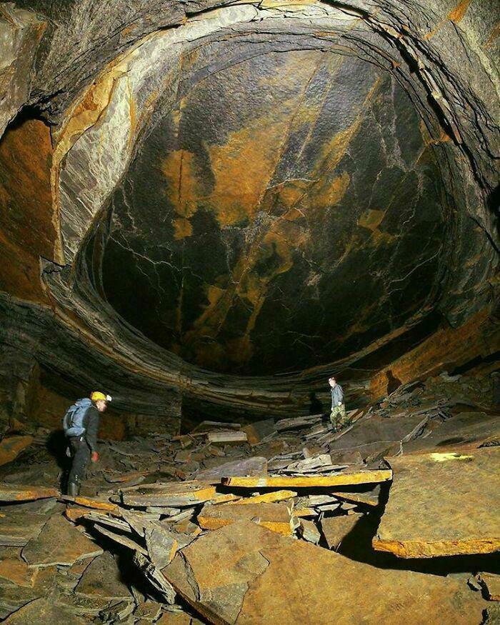 Two people exploring a cave with a large dome-shaped rock formation, illustrating the scale of megalophobia.