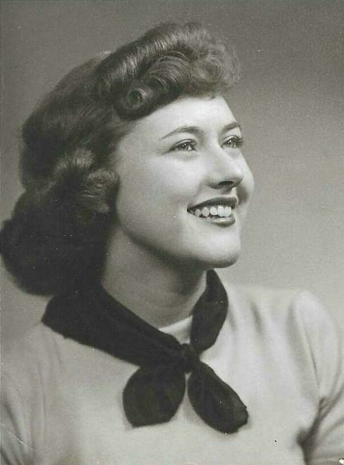 Black and white candid glimpse into the past of a smiling woman with vintage hairstyle and scarf around her neck.
