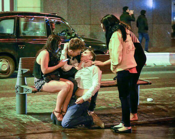 People in street pose evoke accidental Renaissance art with dramatic expressions by a bench at night.