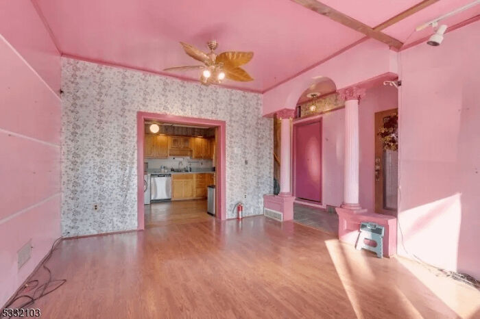 Room with pink walls, floral wallpaper, and wooden flooring showing an example of awful taste but great e*******n.
