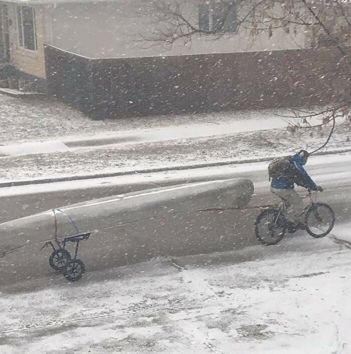 Cyclist towing a canoe on a snowy street, showcasing unique transportation in Canada.