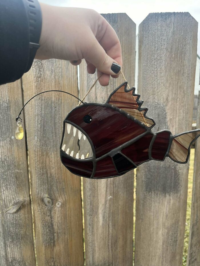 DIY project featuring a stained glass fish sun-catcher held against a wooden fence.