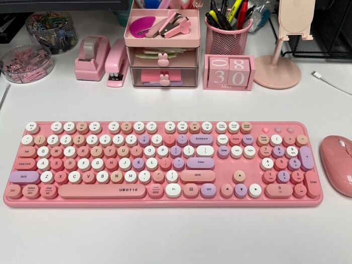 Pink retro keyboard and mouse set on a desk, surrounded by matching pink office supplies, representing impulse buys.