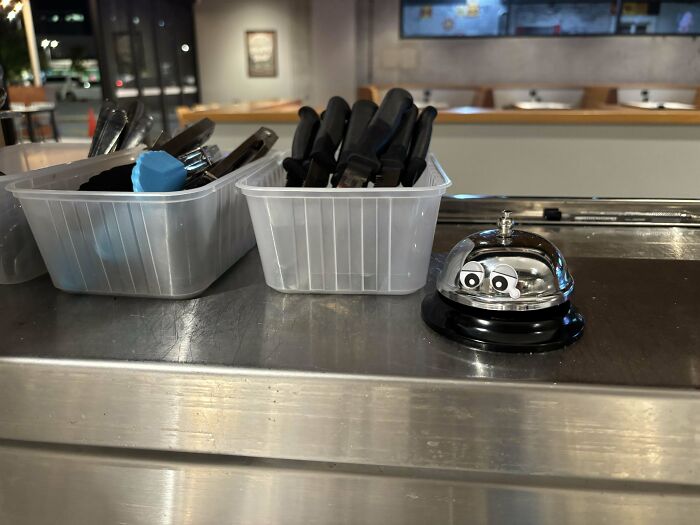 Bell and utensil containers on a counter in a food service setting.