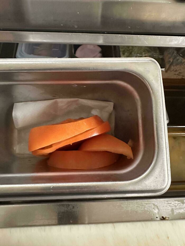 Sliced tomatoes in a metal food service tray, part of a food service industry setup.