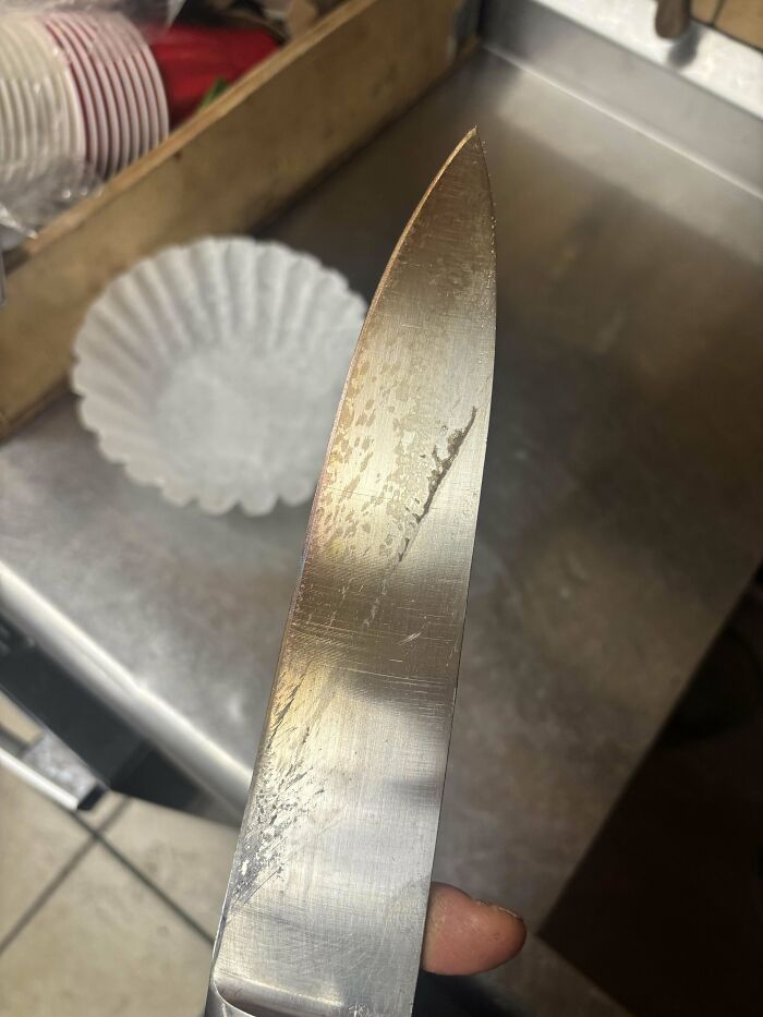 Close-up of a knife in a food service kitchen, showing its sharp, worn blade.