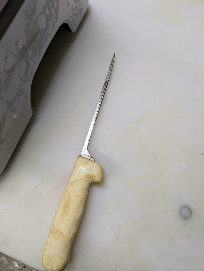 Worn kitchen knife with a beige handle lying on a white surface, representing the food service industry.