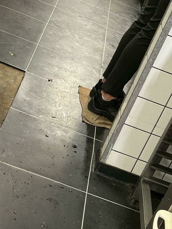 Person standing on a mat in a food service kitchen with wet floors.