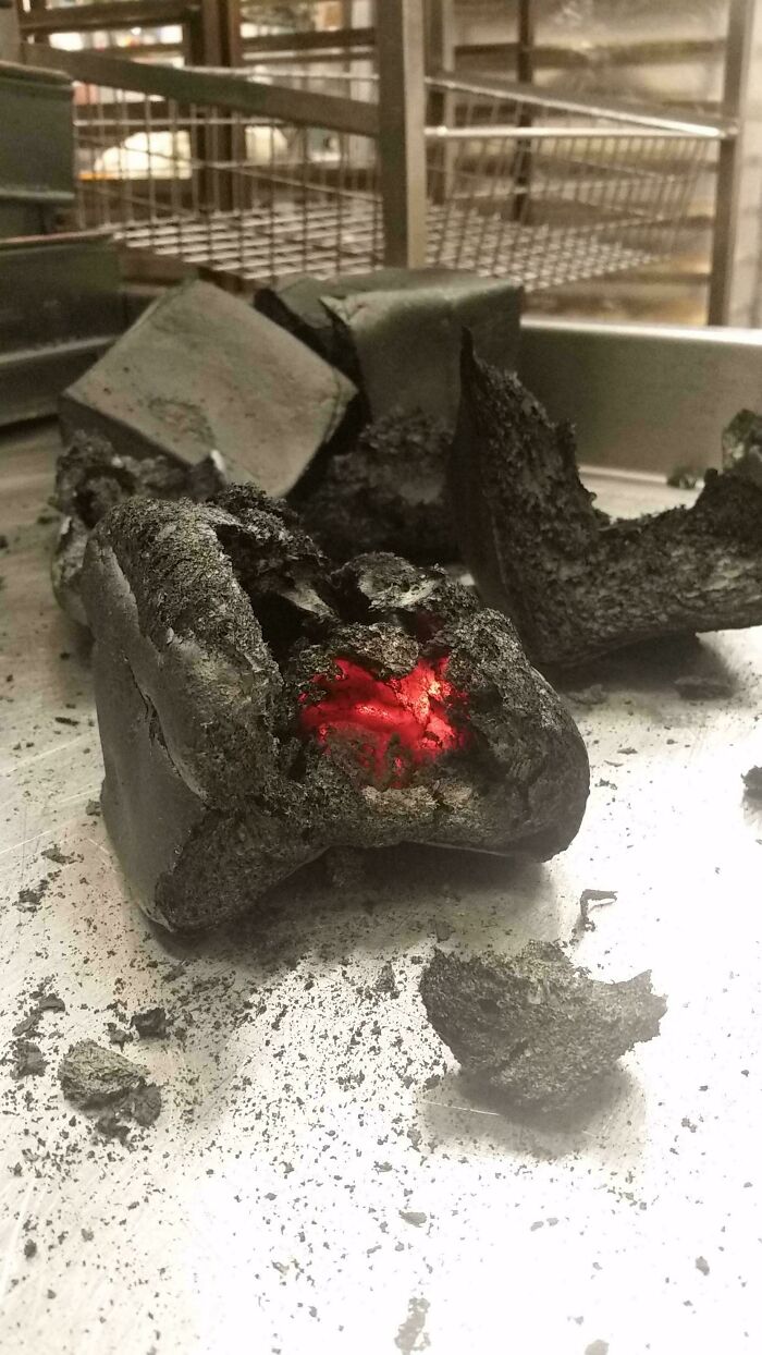 Burnt charcoal briquette in a food service industry setting, glowing red at the center.