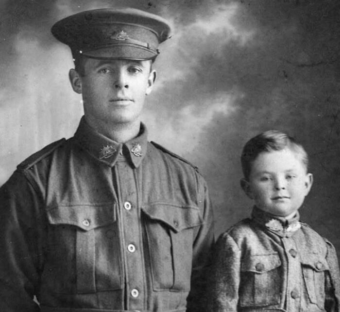 Historic photo of a soldier in uniform with a young boy, both wearing badges, capturing a moment in history.