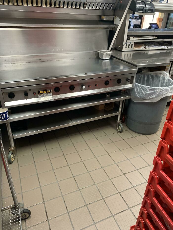 Commercial kitchen setup with grill, utensil, and trash can, typical in food service industry environments.