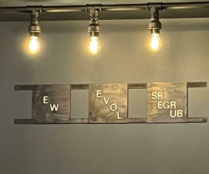 Sign fails with jumbled letters under three light bulbs on a wall.