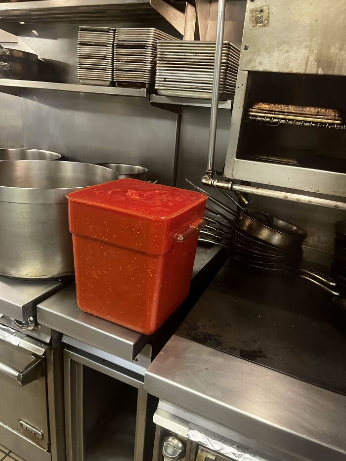 Red container in a busy food service kitchen, surrounded by pots and pans.