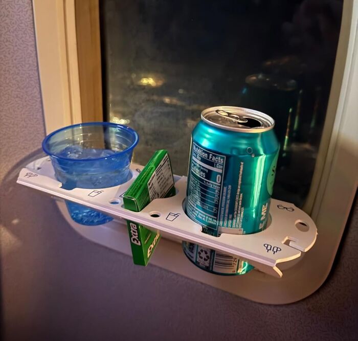Mini travel essentials on a plane window shelf, including a soda can, a cup of ice water, and a pack of gum.