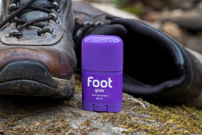 Purple anti-blister balm beside hiking boots, ideal for minimalist carry-on packing.