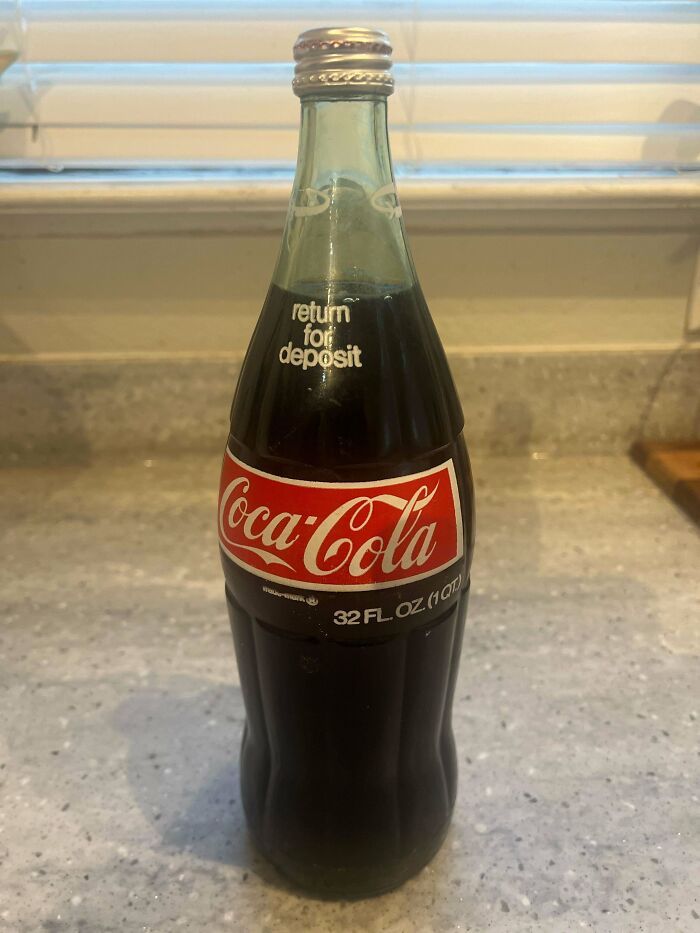 A vintage 32 oz Coca-Cola glass bottle on a countertop, showcasing unique packaging design.