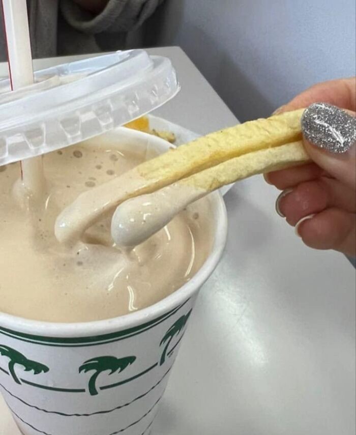 A hand with glittery nails dips fries into a milkshake, capturing a fun girly moment.