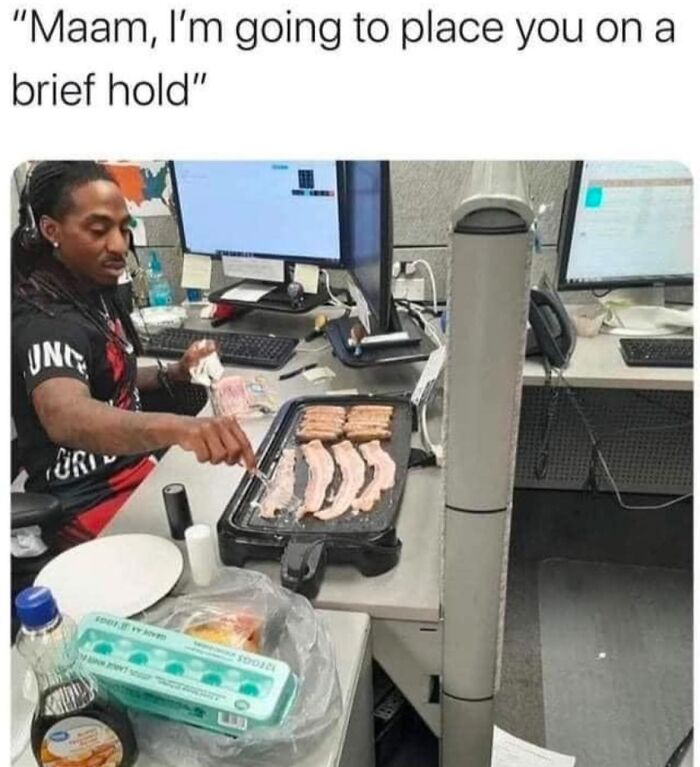 Man cooking bacon at his desk with caption about placing on hold, capturing a "Just Girly Things" meme moment.