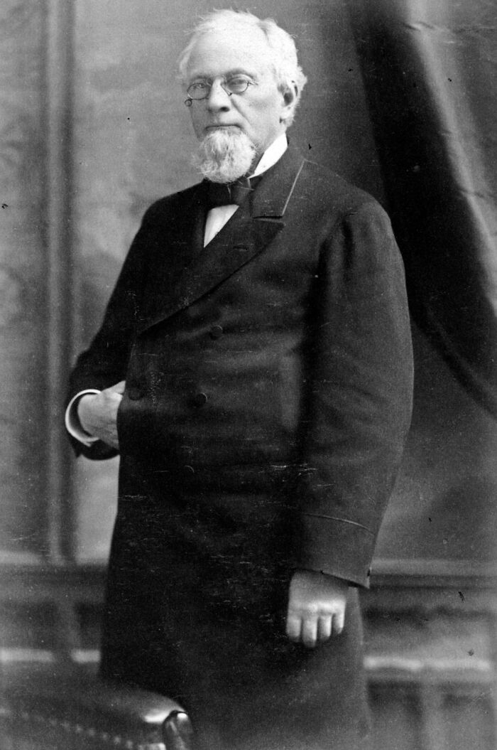 An inventor from the past in formal attire stands with a thoughtful expression.