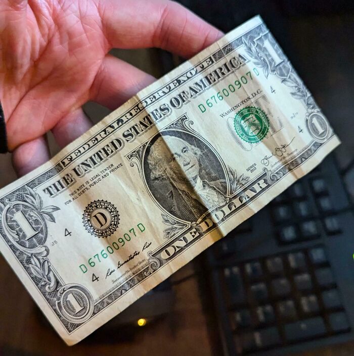 A hand holding a crumpled one-dollar bill over a keyboard, illustrating mildly infuriating server tips.