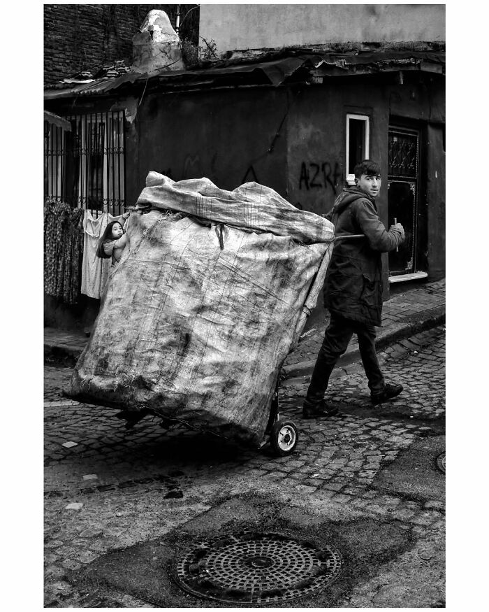 A person pushes a large cart down a cobblestone street in rural Turkey, captured in a striking black-and-white photograph.