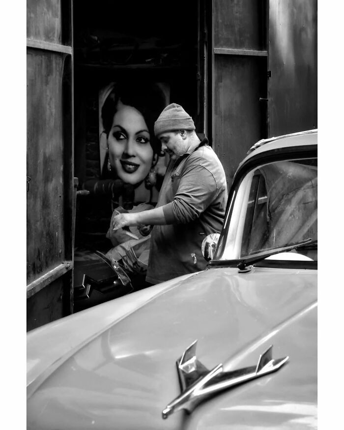 Man working near a vintage car in rural Turkey, with a large black-and-white portrait in the background.