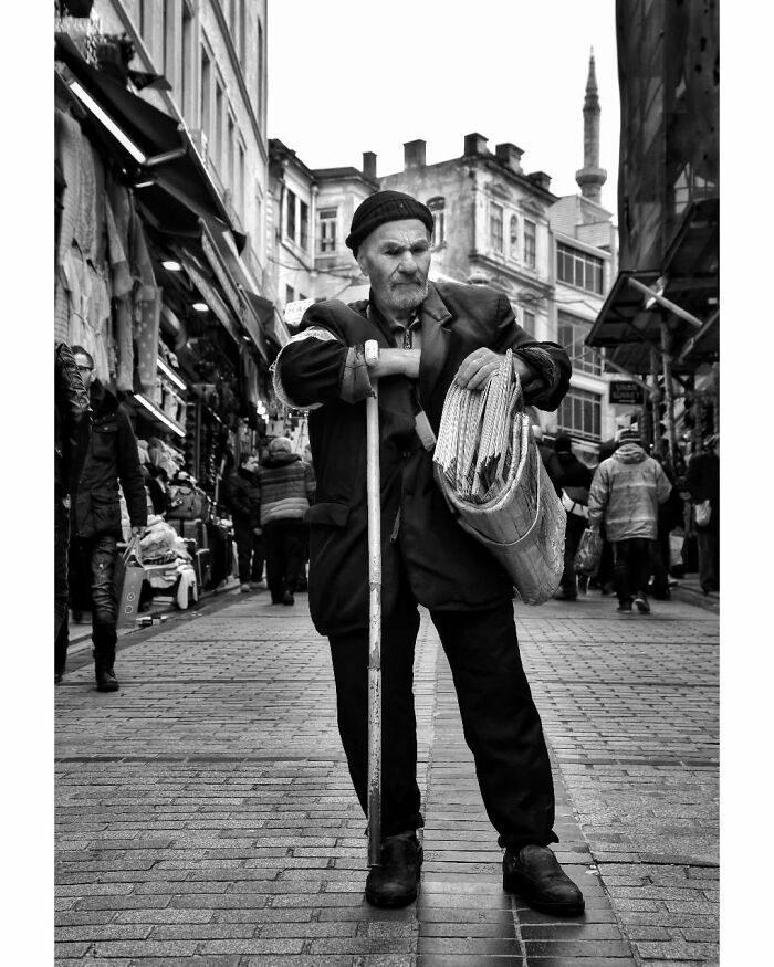 Elderly man with cane and newspapers in black-and-white, on a street scene depicting rural Turkey.