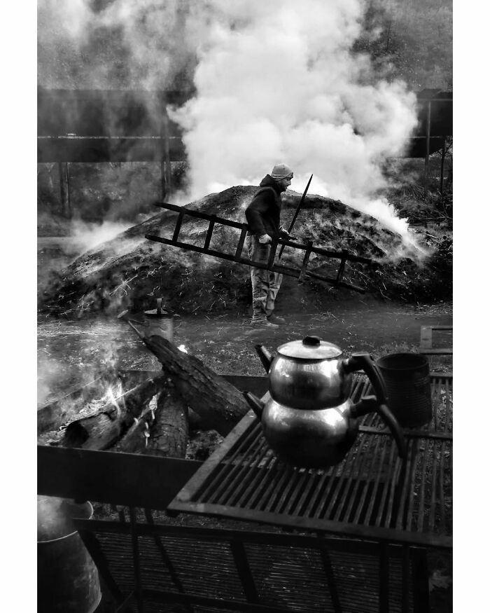 Rural Turkey scene with a man holding a ladder in black-and-white, smoke rising, teapots on an outdoor grill in the foreground.