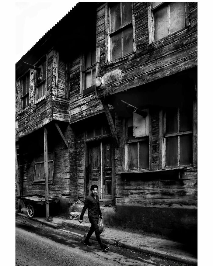 Black-and-white photo of a man walking by an old wooden building in rural Turkey.