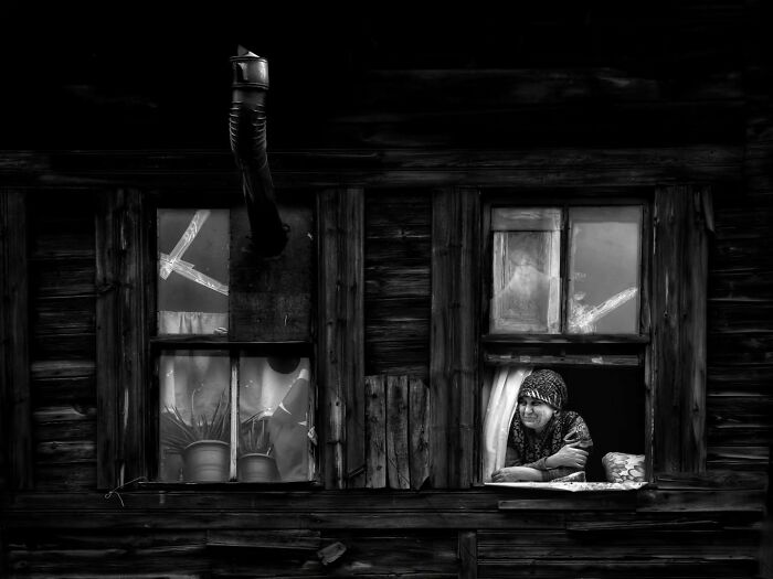 Black-and-white image of a person leaning out a rustic wooden window in rural Turkey.