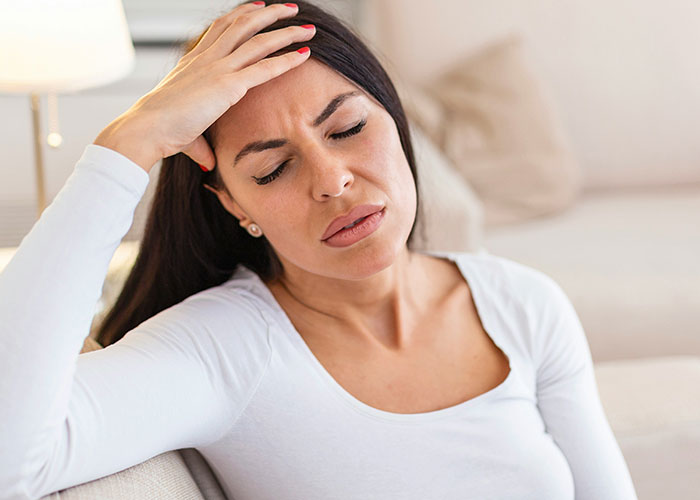 Woman in a white shirt sitting on a couch, appearing contemplative with her hand on her forehead, symbolizing heartfelt last words.