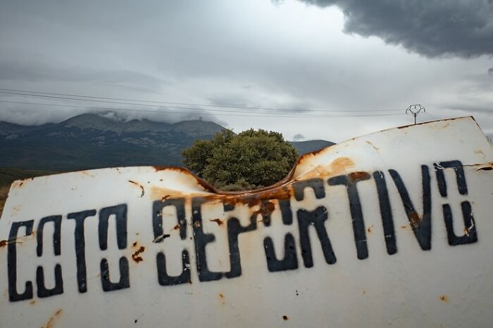Rusty sign with "Coto Deportivo" in front of a misty mountain, creating a striking visual coincidence with a tree.