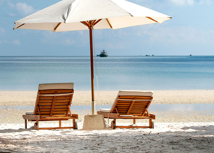 Beach scene with two lounge chairs under an umbrella, reflecting European culture relaxation habits.