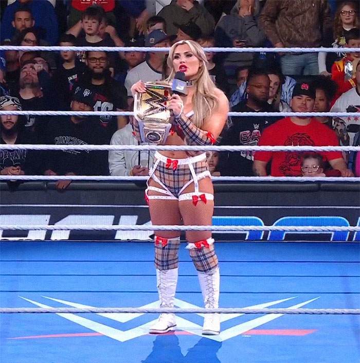 WWE star holding championship belt in ring, with audience in background. WWE star holding championship belt in ring, with audience in background.